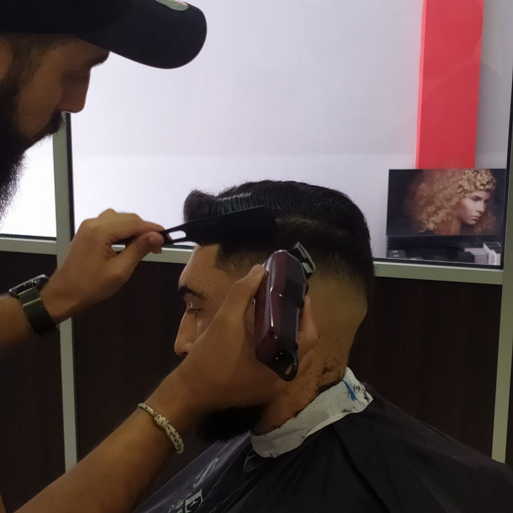 Foto de barbero cortando el pelo con un peine y una máquina clipper wahl